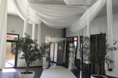 Arc décoratif en fleurs blanches placé dans une salle avec des rideaux gris et un sol en béton.