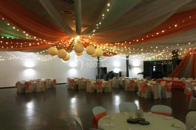 Arc décoratif en fleurs blanches placé dans une salle avec des rideaux gris et un sol en béton.