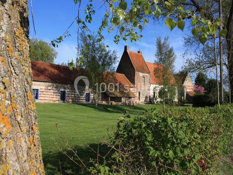 Bâtisse en pierre et briques avec toit en tuiles rouges, entourée d'un jardin verdoyant et d'arbres.