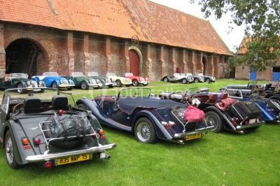 Façade d'une grange en briques avec porte en bois rouge, toit en tuiles et piles de bois empilées sur les côtés.