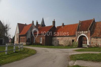 Façade d'une grange en briques avec porte en bois rouge, toit en tuiles et piles de bois empilées sur les côtés.