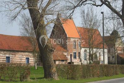 Façade d'une grange en briques avec porte en bois rouge, toit en tuiles et piles de bois empilées sur les côtés.