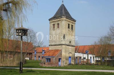 Façade d'une grange en briques avec porte en bois rouge, toit en tuiles et piles de bois empilées sur les côtés.