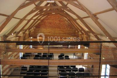 Façade d'une grange en briques avec porte en bois rouge, toit en tuiles et piles de bois empilées sur les côtés.