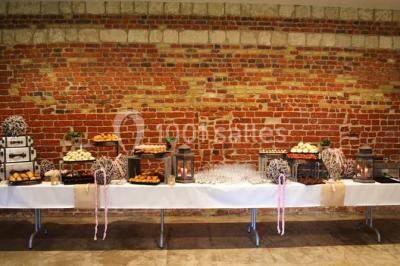 Façade d'une grange en briques avec porte en bois rouge, toit en tuiles et piles de bois empilées sur les côtés.