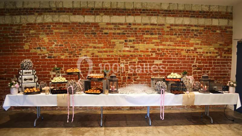 Table de buffet décorée avec des lanternes, des fleurs et des pâtisseries, devant un mur de briques rouges.