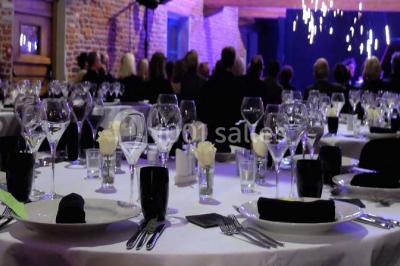 Façade d'une grange en briques avec porte en bois rouge, toit en tuiles et piles de bois empilées sur les côtés.