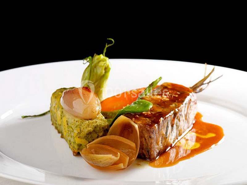 Assiette gastronomique avec viande nappée de sauce, légumes variés et accompagnement vert sur fond noir.