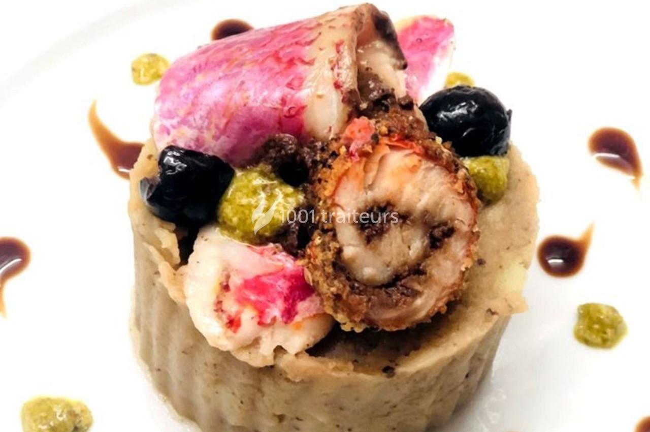 Plat gastronomique composé de poisson, purée, olives noires, pesto et sauce décorative sur une assiette blanche.