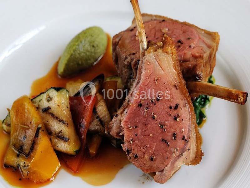 Carré d'agneau rosé avec légumes grillés, purée verte et sauce, présenté sur une assiette blanche.
