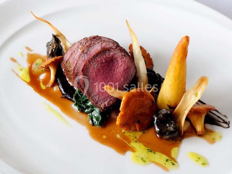 Assiette gastronomique avec viande rouge tranchée, champignons, légumes racines et sauce dressée sur une assiette blanche.