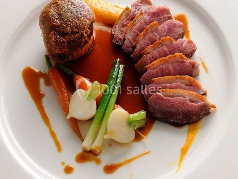Tranches de magret de canard avec légumes glacés, purée et sauce disposés sur une assiette blanche.