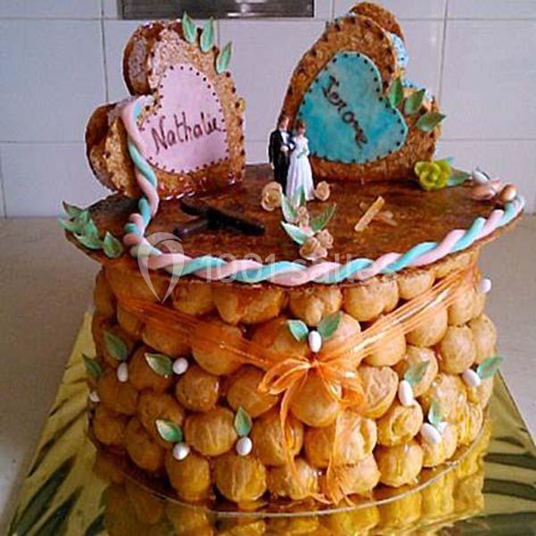 Pièce montée en choux décorée de deux cœurs en sucre avec des prénoms, figurines de mariage et ruban orange.