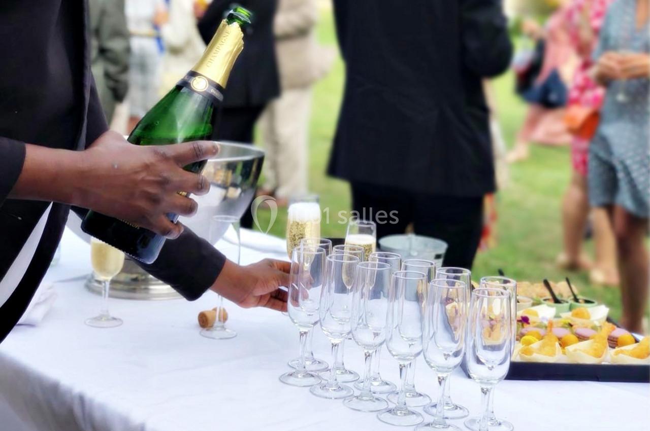 Un serveur verse du champagne dans des flûtes alignées sur une table lors d'un événement en extérieur.