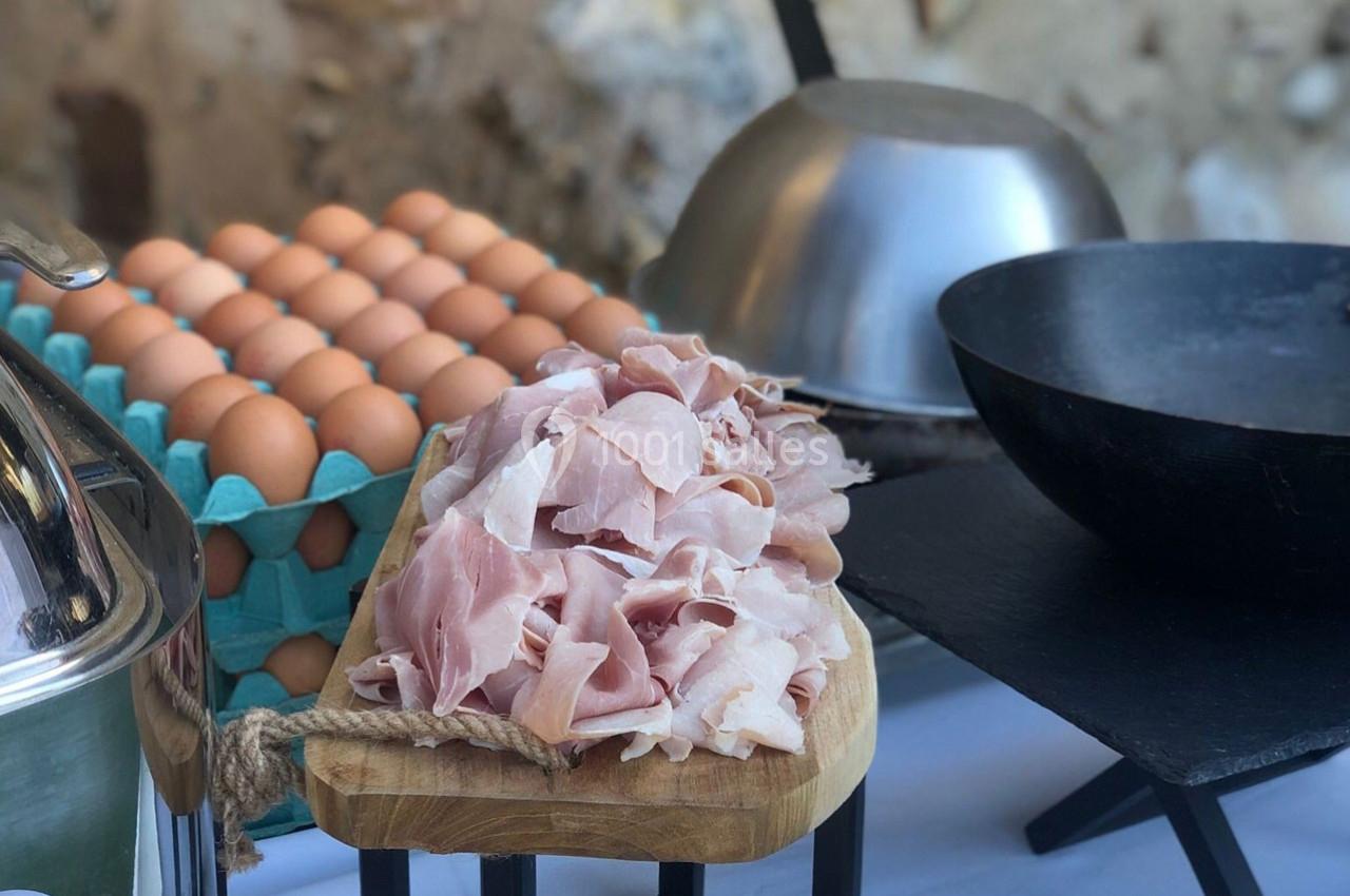 Tranches de jambon sur une planche en bois, posées à côté de boîtes d'œufs et d'ustensiles de cuisine.
