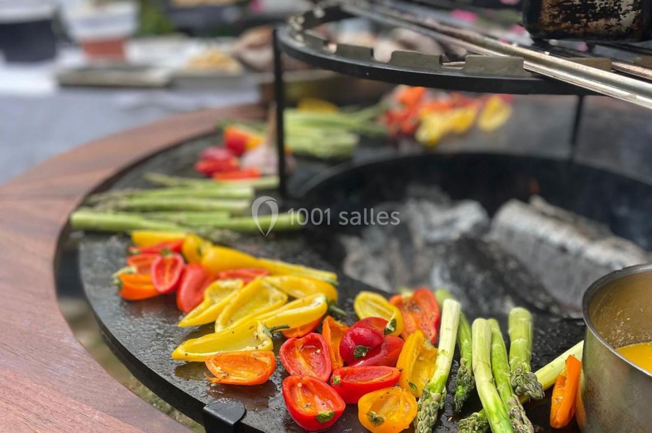 Légumes colorés, dont asperges et tomates, grillant sur une plancha ronde en extérieur.