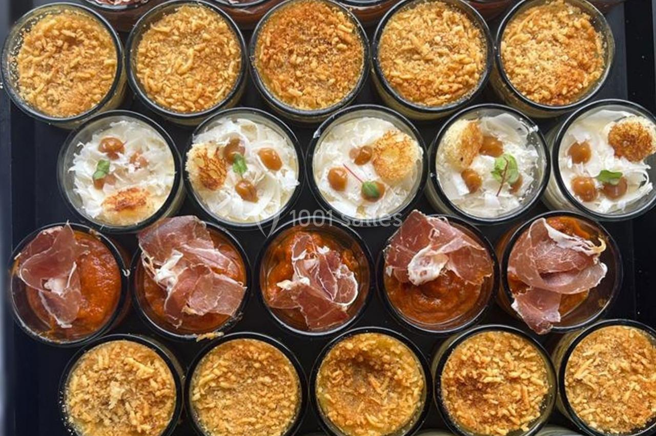 Assortiment de verrines salées garnies de jambon, fromage, sauces et miettes croustillantes, disposées sur un plateau.