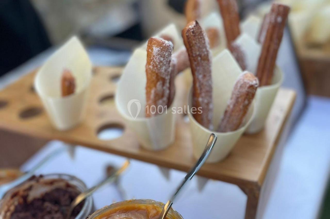 Cônes en papier contenant des churros saupoudrés de sucre, présentés sur un support en bois avec des sauces en premier plan.
