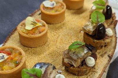 Assortiment de bouchées gastronomiques sur une planche en bois, incluant tartes aux légumes et poissons garnis.
