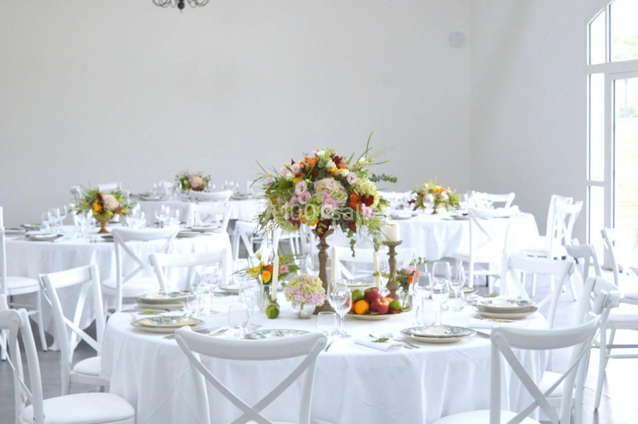 Salle lumineuse avec des tables rondes dressées, décorées de bouquets de fleurs colorées et de vaisselle élégante.