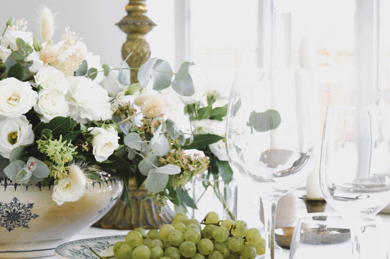 Table élégamment dressée avec assiette de raisins, bouquet de fleurs blanches et chandelier près d'une fenêtre lumineuse.