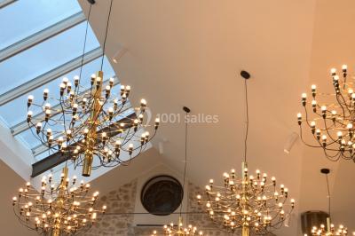 Salle de réception lumineuse avec murs en pierre, tables décorées de fleurs colorées et chandeliers suspendus.