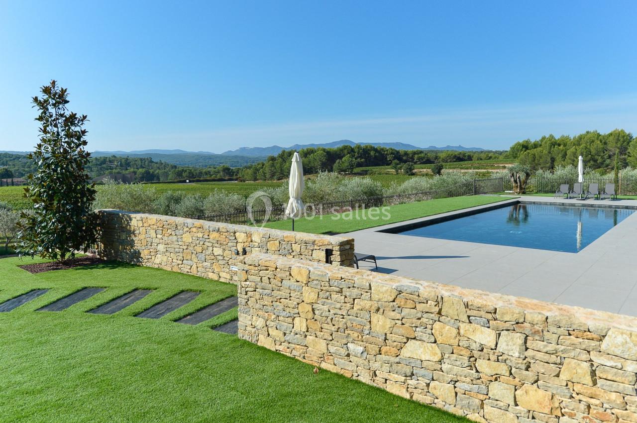 Piscine moderne entourée de pelouse, avec vue sur des champs, des collines et un ciel dégagé.