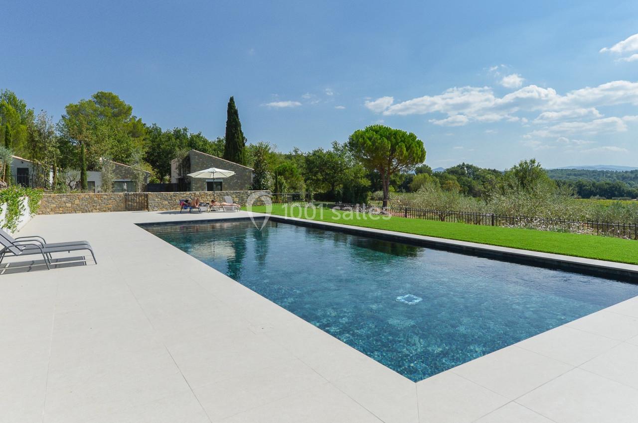 Piscine extérieure rectangulaire entourée de dalles claires, avec vue sur un paysage arboré et colline en arrière-plan.
