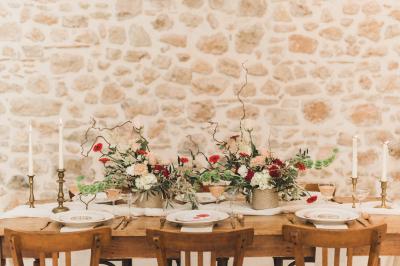 Salle de réception lumineuse avec murs en pierre, tables décorées de fleurs colorées et chandeliers suspendus.