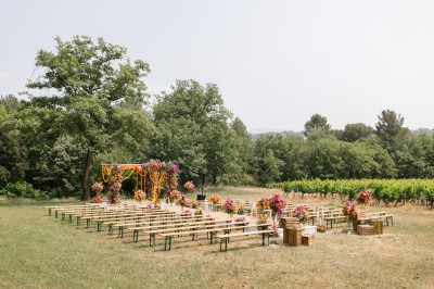 Salle de réception lumineuse avec murs en pierre, tables décorées de fleurs colorées et chandeliers suspendus.