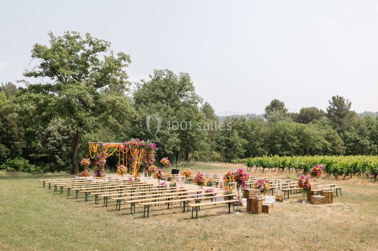 Chaises en bois disposées en rangées devant une arche décorée de fleurs colorées dans un cadre naturel verdoyant.