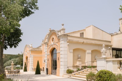 Salle de réception lumineuse avec murs en pierre, tables décorées de fleurs colorées et chandeliers suspendus.