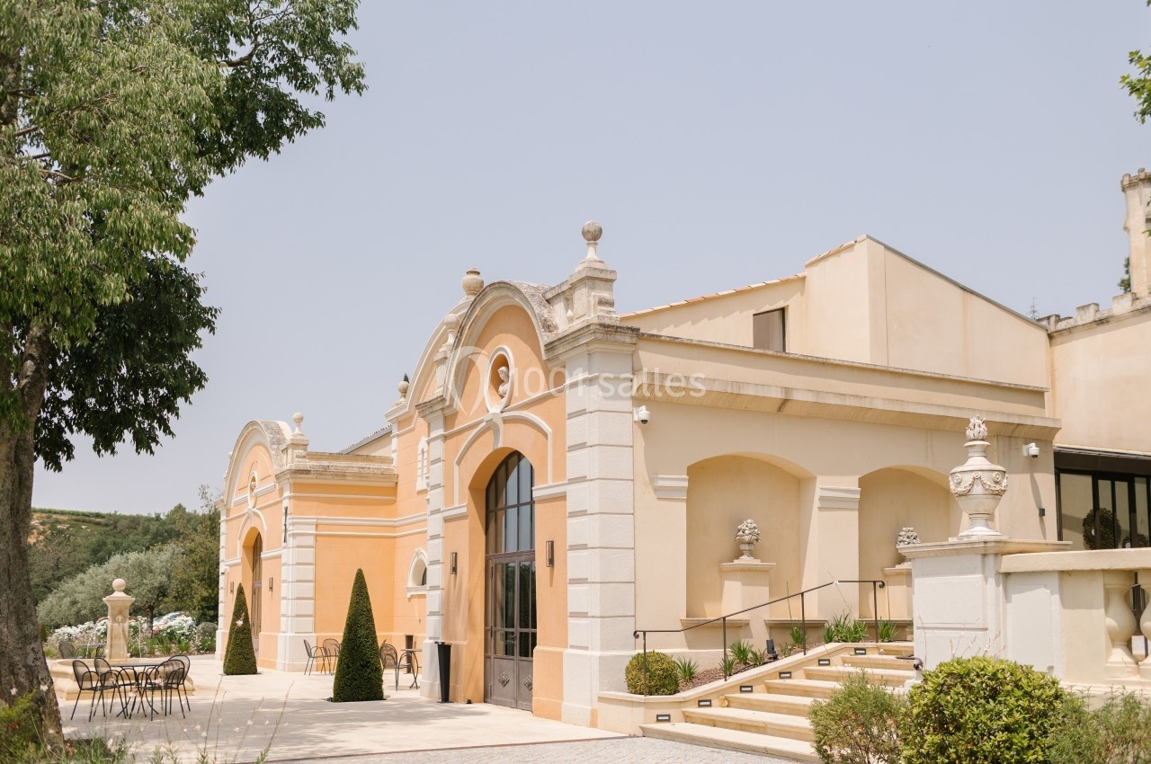 Façade d'un bâtiment élégant de style classique avec arches, entouré de végétation et d'une terrasse aménagée.