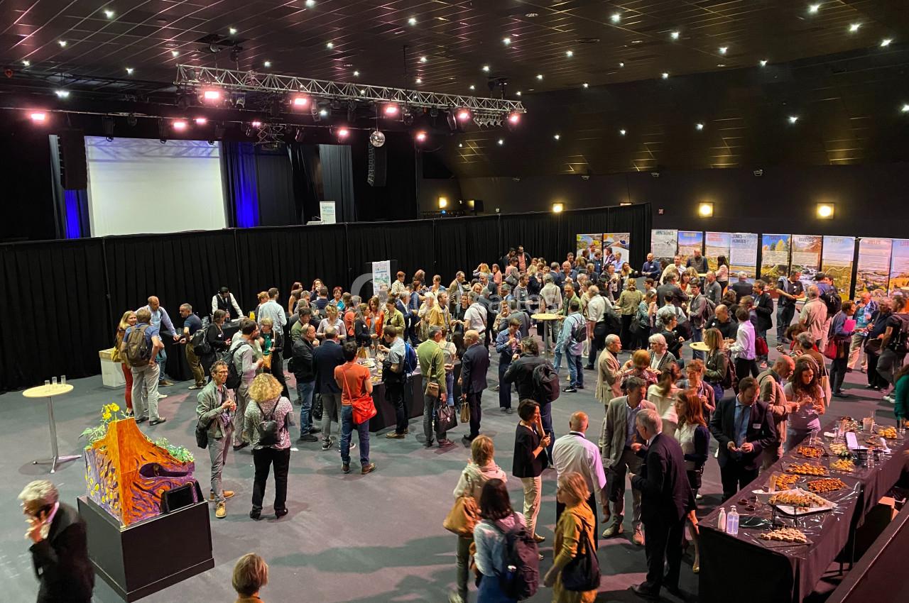 Groupe de personnes rassemblées dans une salle de conférence, discutant près de stands et d'un buffet.