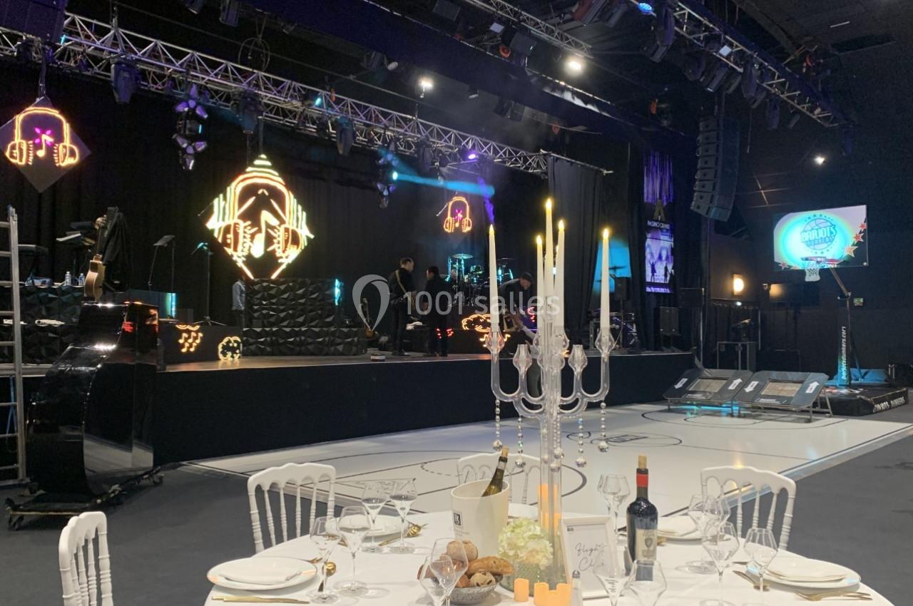 Salle de réception avec scène éclairée, table dressée au premier plan et décorations lumineuses en arrière-plan.