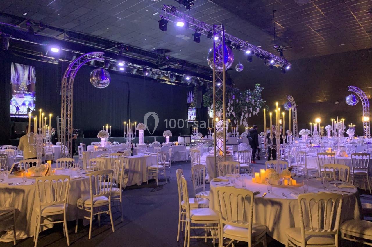 Salle de réception décorée avec des tables rondes, nappes blanches, chandeliers et éclairage tamisé.