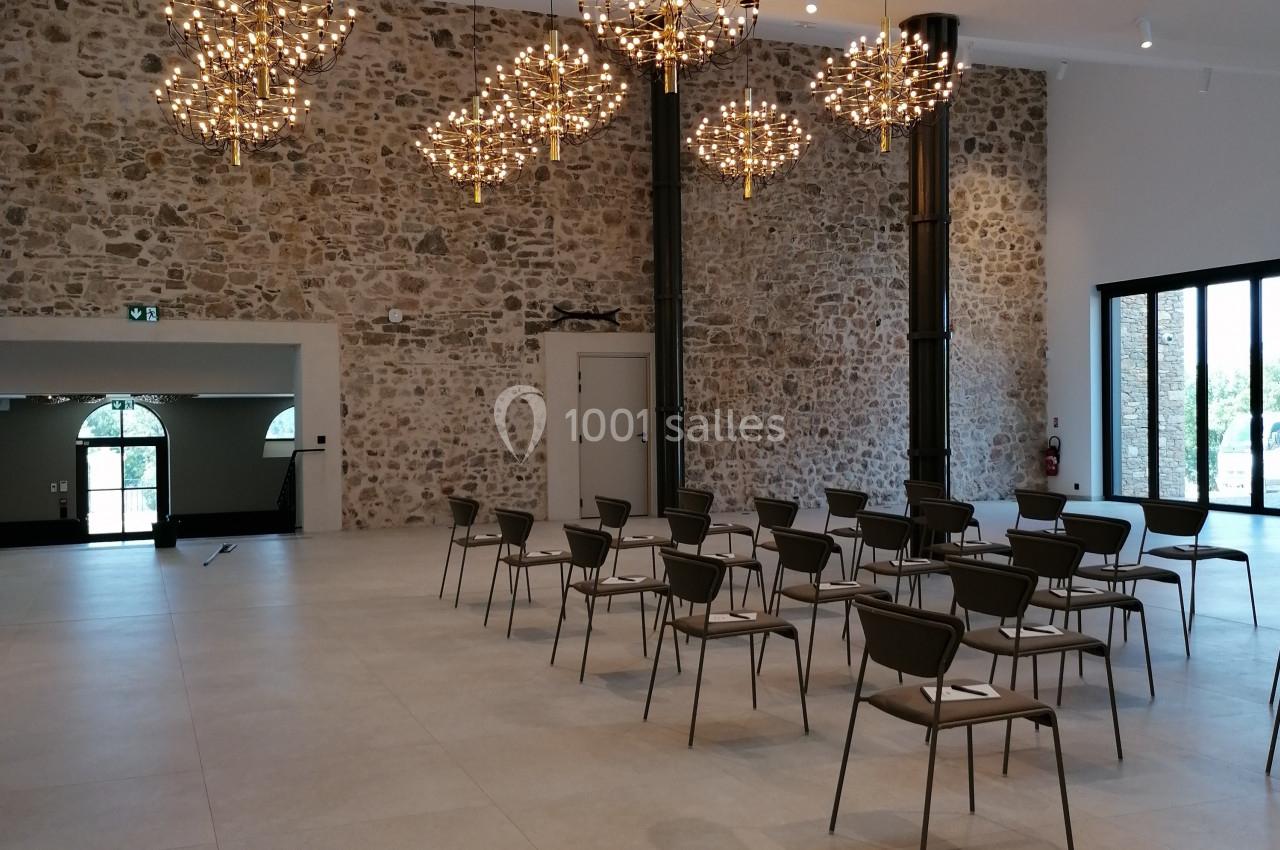 Salle lumineuse avec murs en pierre, chaises disposées en rangées et lustres modernes suspendus au plafond.