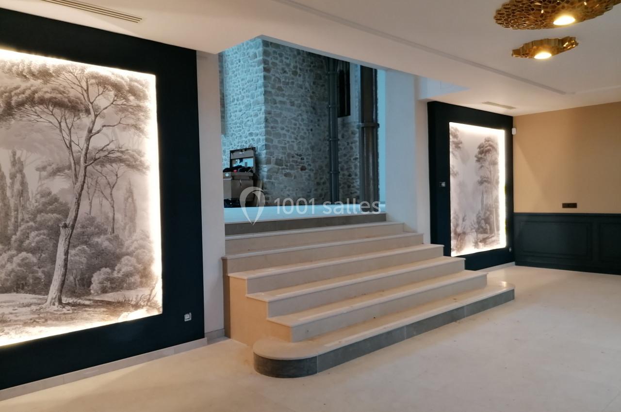 Escalier intérieur en pierre avec éclairage mural mettant en valeur des illustrations de paysages.