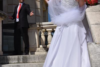 Mannequin vêtu d'une robe en dentelle blanche avec un voile noir couvrant la tête, devant une porte en bois clair.