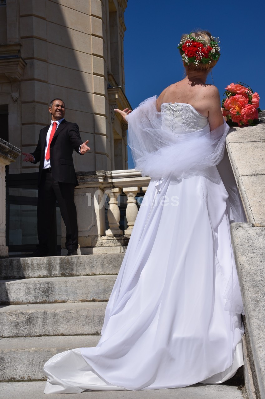 Un homme en costume s'adresse à une femme en robe de mariée sur des marches en pierre devant un bâtiment classique.