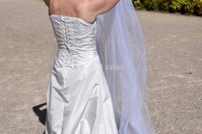 Mannequin vêtu d'une robe en dentelle blanche avec un voile noir couvrant la tête, devant une porte en bois clair.
