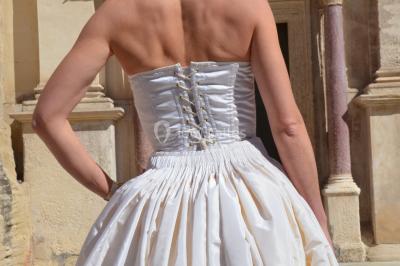 Mannequin vêtu d'une robe en dentelle blanche avec un voile noir couvrant la tête, devant une porte en bois clair.