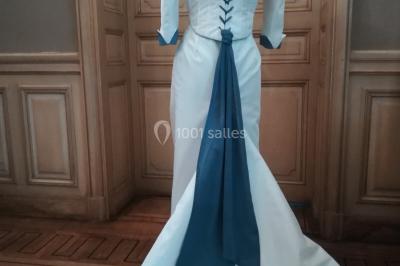 Mannequin vêtu d'une robe en dentelle blanche avec un voile noir couvrant la tête, devant une porte en bois clair.