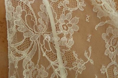 Mannequin vêtu d'une robe en dentelle blanche avec un voile noir couvrant la tête, devant une porte en bois clair.