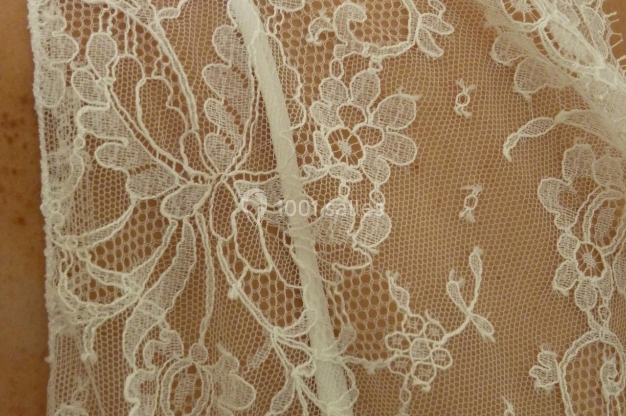 Dentelle blanche délicate avec motifs floraux portée sur une épaule.