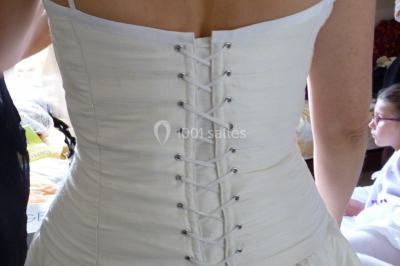 Mannequin vêtu d'une robe en dentelle blanche avec un voile noir couvrant la tête, devant une porte en bois clair.