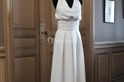 Mannequin vêtu d'une robe en dentelle blanche avec un voile noir couvrant la tête, devant une porte en bois clair.