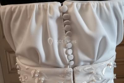 Mannequin vêtu d'une robe en dentelle blanche avec un voile noir couvrant la tête, devant une porte en bois clair.