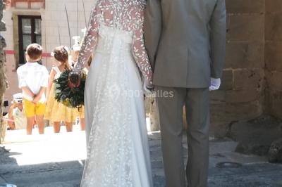 Mannequin vêtu d'une robe en dentelle blanche avec un voile noir couvrant la tête, devant une porte en bois clair.