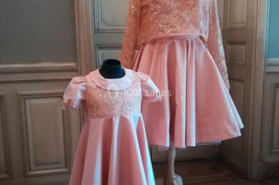 Mannequin vêtu d'une robe en dentelle blanche avec un voile noir couvrant la tête, devant une porte en bois clair.